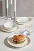 A table setting with a sandwich on a plate, a glass of water, and stacked plates and bowls. Produktbild-Vorschau