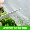 A hand is shown cutting a white mesh fabric with scissors over a bed of green lettuce. Produktbild-Vorschau