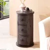 A dark gray cylindrical side table with three drawers sits next to a white sofa in a well-lit room. Náhled obrázku produktu