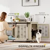 A woman is interacting with a dog crate that has two doors, one sliding and one hinged. A dog is partially inside the crate. Náhled obrázku produktu