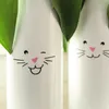 Close-up of two white vases decorated with bunny faces, with green leaves emerging from the top. Náhled obrázku produktu