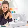 A woman is smiling and holding a pencil next to a sewing machine on a desk. Produktbild-Vorschau