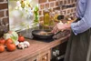 A person is cooking in a kitchen with a backsplash featuring a floral image. Náhľad obrázku produktu
