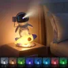 An astronaut figurine on a rocket lamp is placed on a nightstand next to a bed. Náhled obrázku produktu