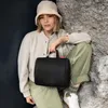 A woman sitting on rocks, holding a black toiletry bag. Anteprima dell’immagine prodotto