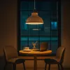 A pendant lamp hangs over a small table with two chairs, a laptop, and a cup of coffee, set against a window at night. Produktbild-Vorschau