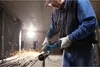 A person is using an angle grinder to cut a metal pipe in what appears to be a construction site. Produktbild-Vorschau