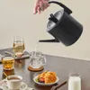 A hand is pouring hot water from a black electric kettle into a glass mug on a table with breakfast items. Podgląd zdjęcia produktu