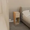 A narrow wooden nightstand with one drawer and an open shelf is placed next to a bed in a bedroom. Produktbild-Vorschau