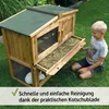 A young boy is kneeling next to a wooden rabbit hutch in a grassy yard, with the hutch's pull-out tray extended. Produktbild-Vorschau