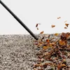 A close-up shot of a leaf blower nozzle blowing leaves off a gravel surface. Anteprima dell’immagine prodotto