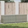 A poly rattan garden box is shown in an outdoor setting, placed on gravel in front of a wooden fence and some greenery. Produktbild-Vorschau