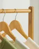 Close-up of wooden hangers on a bamboo rack, with some clothing items visible. Produktbild-Vorschau