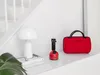 A red portable steamer and a white lamp are displayed on a white shelf next to a staircase. Produktbild-Vorschau