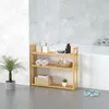 A three-tiered wooden shelf unit in a bathroom, holding various toiletries and towels. A palm plant is beside it, and a bathtub is in the background. Produktbild-Vorschau