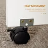 A close-up of a caster wheel with a brake attached to the bottom of a white furniture piece, resting on a carpeted floor. Text overlays describe the product's features. Produktbild-Vorschau