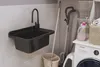 A laundry room or utility area with a sink, washing machine, and cleaning supplies. Anteprima dell’immagine prodotto