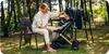 A woman is sitting on a chair next to a baby stroller in a garden setting. Produktbild-Vorschau