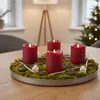 An advent wreath with four red LED candles on a wooden table, with a lamp and a Christmas tree in the background. Produktbild-Vorschau