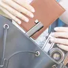 A person is placing a USB hub into a bag, alongside a wallet and a camera. Produktbild-Vorschau