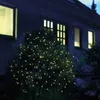 A bush decorated with small, warm white LED lights at night, with a house in the background. Produktbild-Vorschau