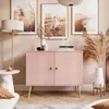 A pink two-door cabinet with wooden legs, decorated with dried flowers and artwork in a room. Produktbild-Vorschau