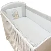 A baby crib with bedding, including a bumper and a pillow with a teddy bear design. Produktbild-Vorschau