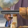 A close-up of a person's hands using a wood lathe to shape a piece of wood. Náhled obrázku produktu