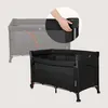 A hand is shown pressing a button on a black travel crib, demonstrating how to fold it. A faded image of the crib in its unfolded state is in the background. Voir les images du produit