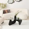 A modern living room scene featuring a fluffy white couch and a unique black coffee table with a glass top. Produktbild-Vorschau