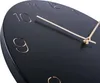 A close-up view of a black wall clock with gold numbers and hands. Produktbild-Vorschau
