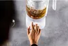 A hand is pressing a button on a white electric kettle filled with a brown liquid. Náhled obrázku produktu