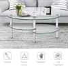 A glass coffee table with a metal frame is shown in a living room setting, placed on a striped rug in front of a sofa. Decorative items like books, a vase with flowers, and picture frames are on the table. Náhľad obrázku produktu