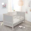 A baby crib in a nursery setting with artwork on the wall and a rug on the floor. Produktbild-Vorschau