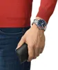 A person wearing a red sweater and blue jeans, with a watch on their wrist and holding a black wallet. Podgląd zdjęcia produktu