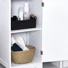 A white bathroom cabinet with two shelves. The top shelf contains a black felt basket with various toiletries. The bottom shelf holds a woven basket filled with folded towels. Produktbild-Vorschau
