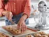 A person is taking cookies off a baking sheet using a spatula next to a stand mixer. Produktbild-Vorschau