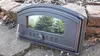 A cast iron oven door with a glass window, placed on stones and dirt. Produktbild-Vorschau