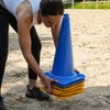 A person is stacking blue and yellow training cones on a sandy surface. Náhľad obrázku produktu