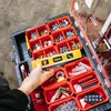A hand is shown organizing tools in a red and black tool organizer box. Náhled obrázku produktu