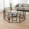 A black metal dog playpen is set up in a living room with a couch and plant in the background. Inside the playpen are dog toys, a dog bed, and food bowls. Náhled obrázku produktu