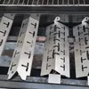Four metal heat shields are arranged in a row on a grill. Produktbild-Vorschau