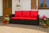 A black outdoor sofa with red cushions sits on a paved patio in front of a white house with wooden doors and shutters. Potted flowers are placed around the sofa. Produktbild-Vorschau