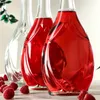 Three glass bottles, two filled with red liquid and one empty, are arranged diagonally on a light-colored surface. Several raspberries are scattered in the foreground. Voir les images du produit