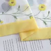 Close-up of a sheer curtain with embroidered yellow daisies and a yellow band, laid over a page of text. Produktbild-Vorschau