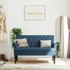 A blue loveseat with tufted backrest is placed in a hallway with a coat, shoes, a plant, a framed picture, and a mirror. Náhled obrázku produktu