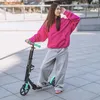 A young woman stands with a scooter in an urban outdoor setting. Produktbild-Vorschau