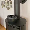 A black cast iron humidifier sits on top of a black wood-burning stove, with a wall of framed pictures in the background. Produktbild-Vorschau