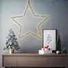 A festive Christmas display on a wooden console table, featuring a flocked artificial tree, decorative gifts, and miniature Christmas trees, all set against a gray wall with a large illuminated star. Anteprima dell’immagine prodotto