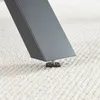 A close-up shot of the bottom of a black metal table leg with an adjustable foot resting on a textured white carpet. Podgląd zdjęcia produktu